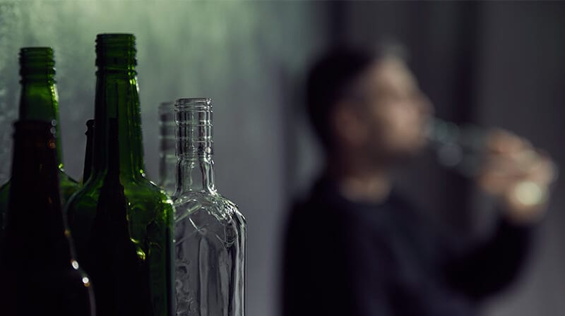 man near alcohol bottles struggling with an alcohol addiction