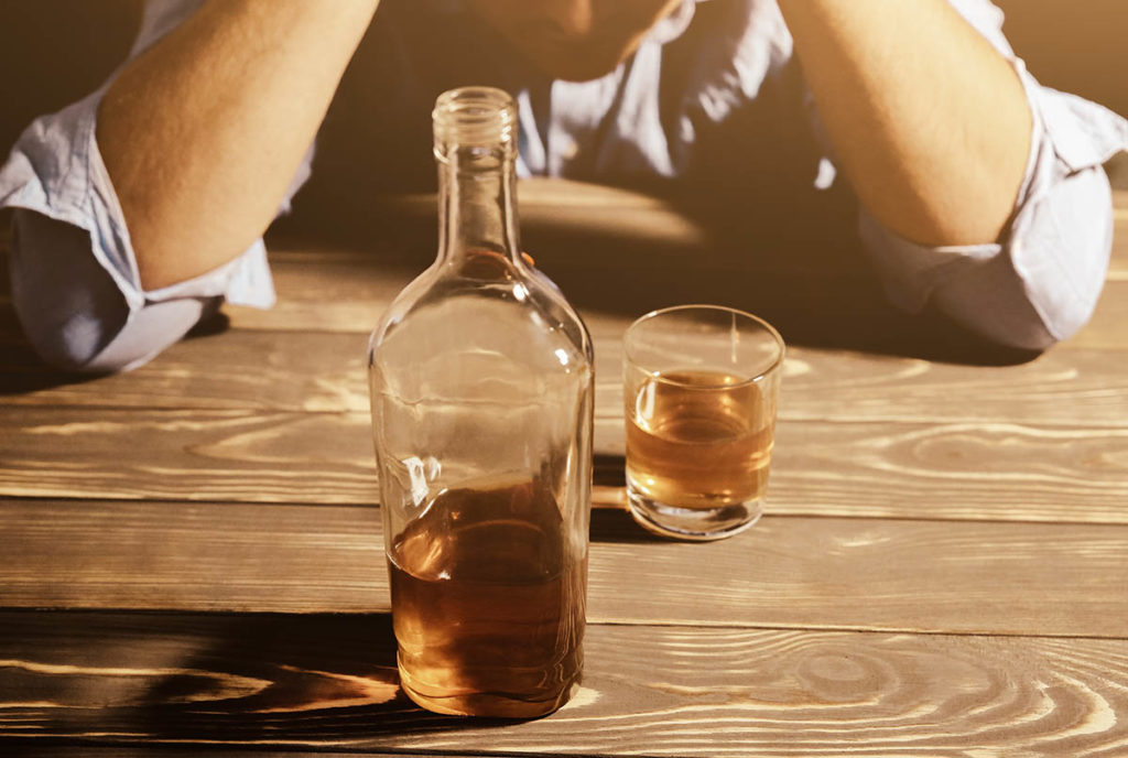 a person drinking a bottle of whiskey by themselves showing signs of alcoholism