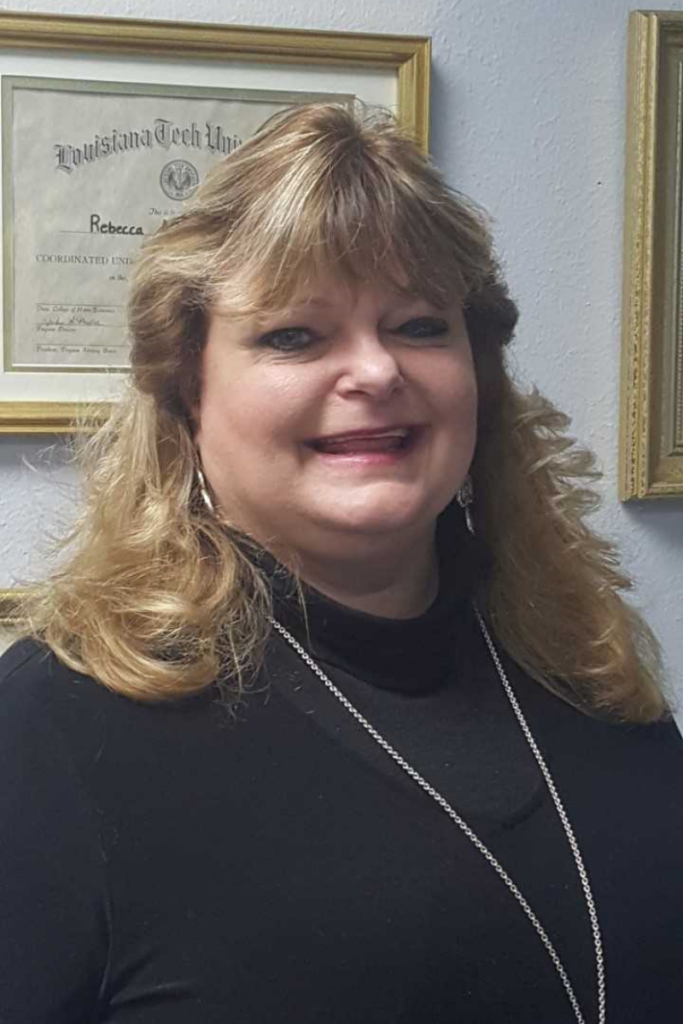 A woman with blonde hair wearing a black top and necklace stands indoors in front of a framed certificate, introducing Becky Laskowski, a licensed professional counselor.