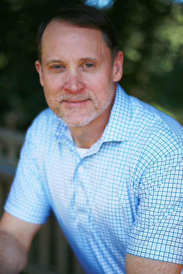 A middle-aged man with short hair and a beard, identified as Michael McCormick, MD and ABAM Certified, wears a blue and white checkered shirt while posing outdoors with greenery in the background.