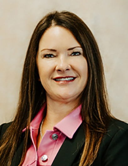 Hollye Rogers, LCSW-BACS, with straight brown hair, wears a black blazer over a pink collared shirt and smiles at the camera against a neutral background.
