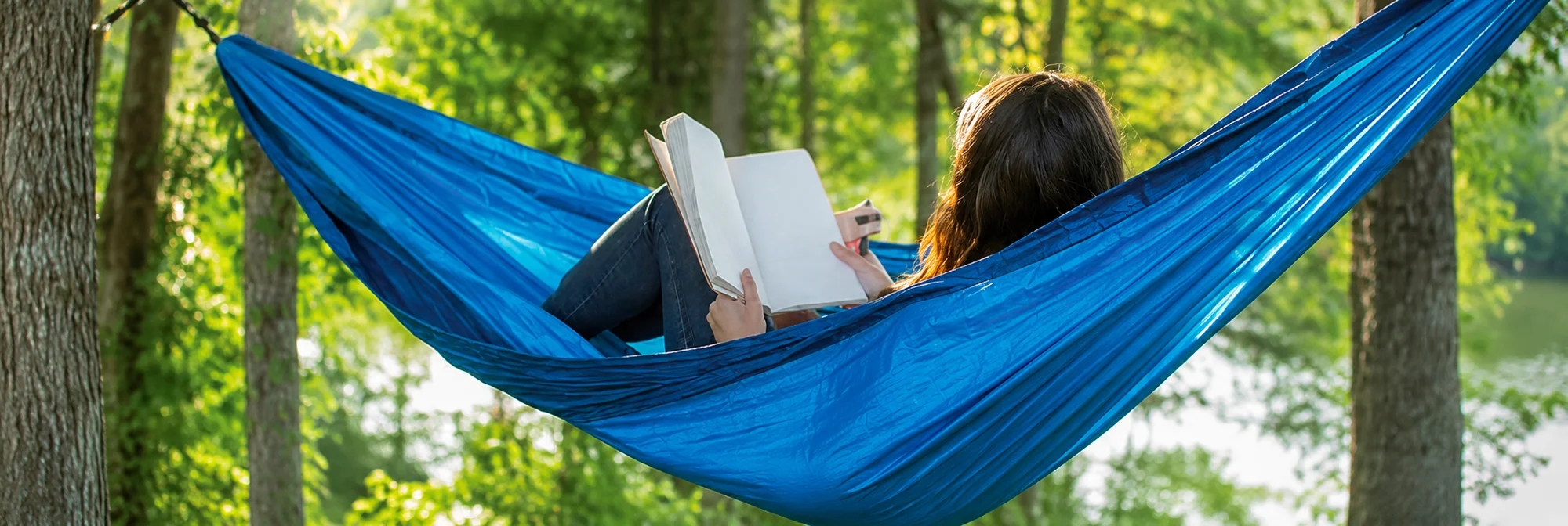 Woman reading a book in a hammock with trees in the background